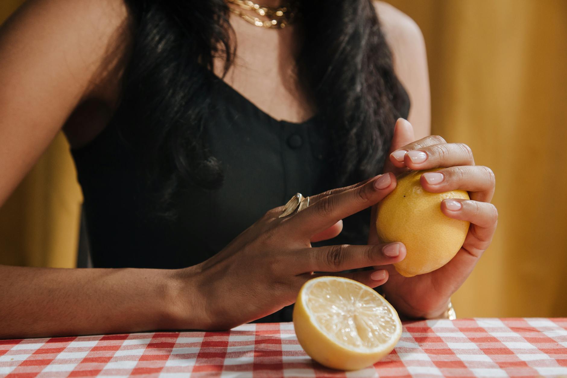 A woman holding a fresh lemon at a dining table, symbolizing the freshness and intentionality of slowing down intimate moments.