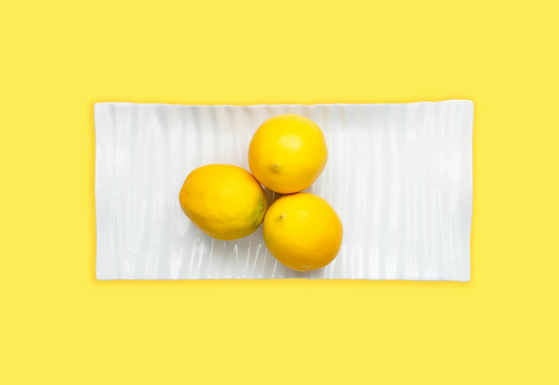 Fresh lemons arranged on white plate with vibrant yellow background, symbolizing renewed pleasure and vitality after 40.