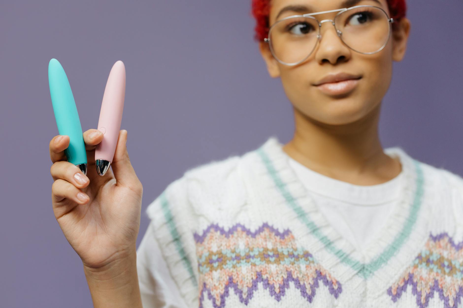 Two colorful vibrators held up against a purple background, representing intimate wellness tools.