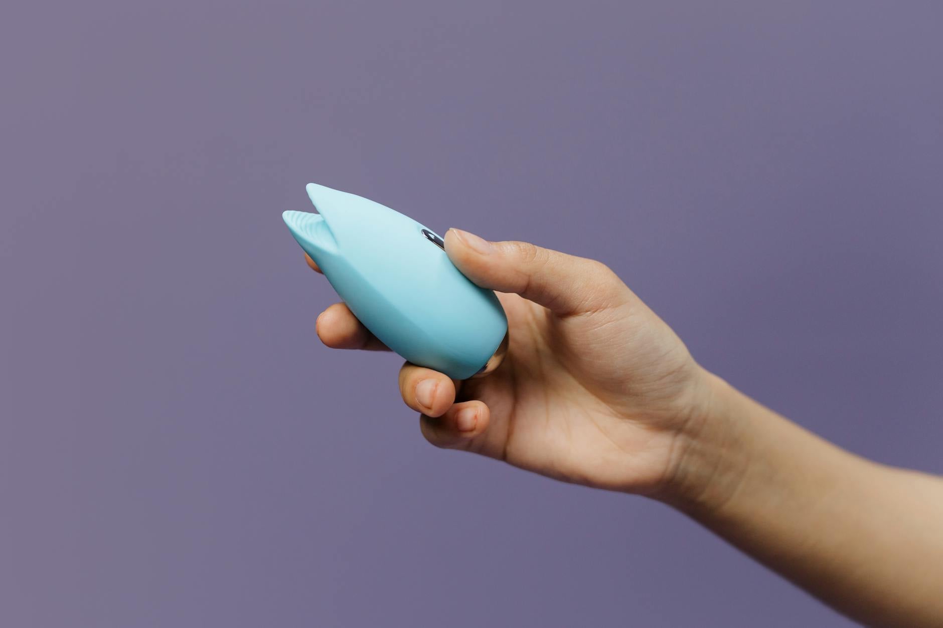 A blue silicone clitoral vibrator held gently in hand, symbolizing gentle pleasure and self-care during recovery